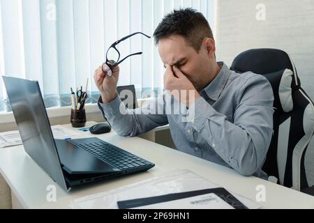 Geschäftsleute, die im Büro arbeiten und Schmerzen am Kopf haben, weil sie am Schreibtisch arbeiten und den ganzen Tag mit einem Laptop sitzen und Kopfschmerzen haben, kranke Mitarbeiter überarbeiten Stockfoto