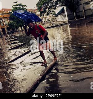 Ein afro-kolumbianischer Mann läuft über die Straße, von sintflutartigen Regenfällen überflutet während der jährlichen Regenzeit in Cartagena, Kolumbien. Stockfoto