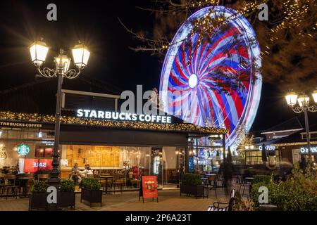 Eintritt für Starbucks Kaffee im Designer Outlet mit weihnachtsdekorationen während der Nacht. Riesenrad im Hintergrund Stockfoto