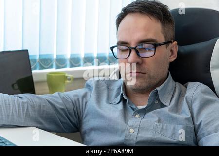 Junger Geschäftsmann in blauem Hemd, der auf dem Schreibtisch im Büro schläft Stockfoto