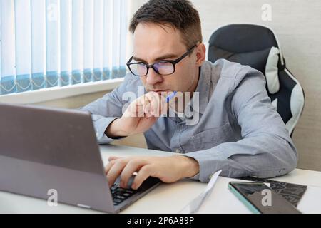 Portrait seines attraktiven, fokussierten professionellen Mannes, der per Fernzugriff eine unterstützende Website programmiert, an einem modernen Arbeitsplatz Stockfoto