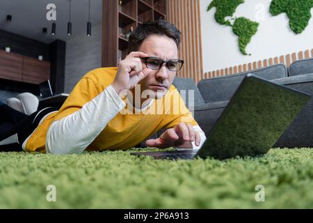 Mann lag auf dem Boden mit Laptop. Ein Freiberufler arbeitet von zu Hause aus. Rücksichtsvoller Kerl Stockfoto