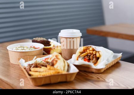 Griechisches Fast-Food-Abendessen in recyclingfähigem Geschirr auf dem Tisch. Souvlaki, Gyros, Pommes Frites und Salat in Einwegtellern Stockfoto