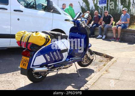 Motorroller warten auf ihre Zeit mit der Fähre, während sie das GP-Modell der SIL Lambretta Serie 3 mit Rennfarbe und voll abgestimmtem Motor aus dem Jahr 1986 bewundern, August 2022. Stockfoto