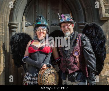 Porträt eines stilvollen Steampunk-Paares mittleren Alters, das schwarze Engelsflügel trägt und vor einer großen gotischen Tür steht. Stockfoto