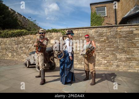 Steampunks richten ihre Waffen auf die Kamera. Ein weiblicher Steampunk trägt einen großen Kupferoktopus auf dem Rücken. Stockfoto