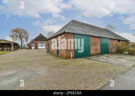 Ein Ziegelgebäude mitten auf einem leeren Grundstück mit zwei Garagen auf der einen Seite und einer anderen dahinter Stockfoto