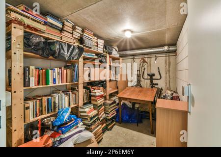 Ein Zimmer mit vielen Büchern auf den Regalen und eine offene Tür, die zu einem anderen Zimmer führt, das voller Sachen ist Stockfoto