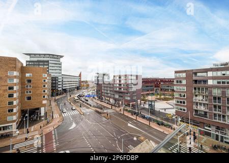 Amsterdam, Niederlande - 10. April 2021: Eine Stadtstraße mit Autos und Menschen auf der Straße, die von einer überquerenden Brücke mit Blick auf einige Gebäude genommen wird Stockfoto