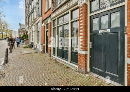 Einige Leute gehen die Straße entlang vor einem alten Ziegelgebäude mit Fensterläden auf beiden Seiten und offenen Türen Stockfoto