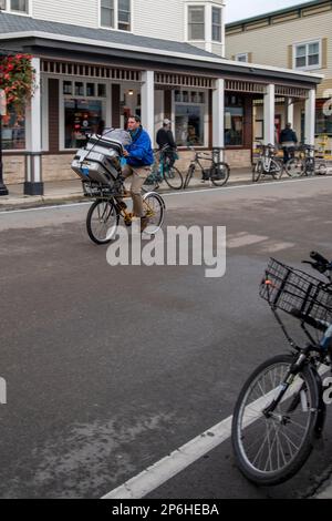 Mackinac Island, Michigan. Auf der Insel sind nur Pferde und Fahrräder erlaubt. Mann auf dem Fahrrad, der Gepäck für das Hotel vor Ort liefert. Stockfoto