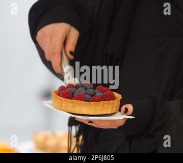 Nahaufnahme eines Verkäufers an einem Konditorstand, der eine Torte an einem kalten Wintertag auf ein Papierfach auf dem Prager Bauernmarkt kauft. Stockfoto