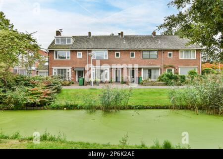 Amsterdam, Niederlande - 10. April 2021: Ein Haus inmitten eines Gartens mit Wasser und Pflanzen an einem sonnigen Tag Stockfoto
