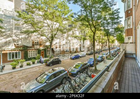 Amsterdam, Niederlande - 10. April 2021: Stadtstraße mit geparkten Autos und Fahrrädern auf dem Gehweg vor einem Apartmentgebäude, umgeben von Bäumen Stockfoto