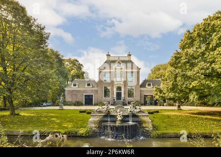 Ein großes Haus mit einem Springbrunnen vorne und Bäumen umgebend an einem sonnigen, blauen bewölkten Himmel Stockfoto