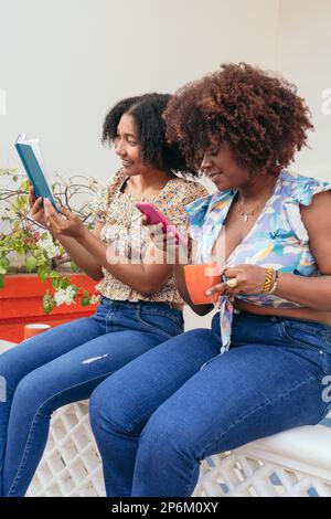 Junge Frauen lesen und telefonieren während der Kaffeepause Stockfoto