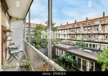 Amsterdam, Niederlande - 10. April 2021: Balkon mit einigen Pflanzen und Gebäuden im Hintergrund, aus dem oberen Fenster eines Apartments zu sehen Stockfoto