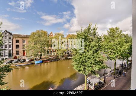 Einige Gebäude und Boote im Wasser mit Bäumen auf beiden Seiten des Flusses, aus Sicht eines Apartmentgebäudes Stockfoto