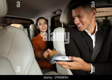 Junge Frau, die den Service mit Kreditkarte über den Zahlungsterminal in einem modernen Taxi bezahlt Stockfoto