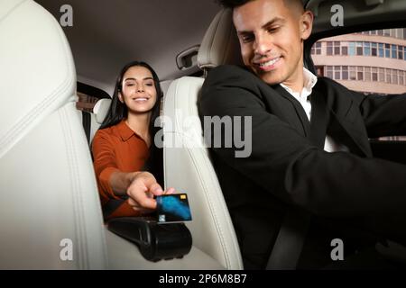 Junge Frau, die den Service mit Kreditkarte über den Zahlungsterminal in einem modernen Taxi bezahlt Stockfoto