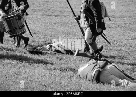Schauspieler in historischen Kostümen erscheinen auf dem Schlachtfeld verletzt oder tot, während andere Soldaten während einer Nachstellung des Revolutionskriegs über sie laufen Stockfoto