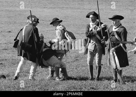 Schauspieler in historischen Kostümen erscheinen auf dem Schlachtfeld verletzt oder tot, während andere Soldaten während einer Nachstellung des Revolutionskriegs über sie laufen Stockfoto