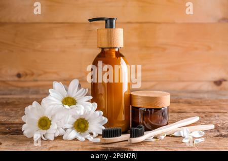 Natürliche Kosmetikprodukte, Zahnbürsten und Kamillenblumen auf Holzhintergrund Stockfoto