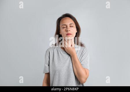 Reife Frau, die Schilddrüsen-Selbstuntersuchung vor hellem Hintergrund durchführt Stockfoto