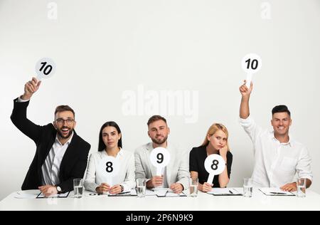 Jury-Gruppe mit unterschiedlichen Punktezeichen am Tisch auf weißem Hintergrund Stockfoto