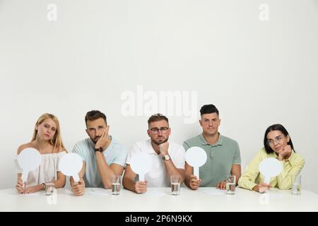 Eine Gruppe enttäuschter Juroren, die am Tisch auf weißem Hintergrund ein Blankozeichen halten. Platz für Text Stockfoto