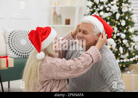 Glückliches, reifes Paar in Weihnachtsmannhüten zu Hause. Weihnachtsfeier Stockfoto