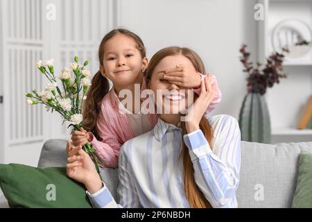 Ein kleines Mädchen mit Blumen, das zu Hause die Augen seiner Mutter schließt Stockfoto