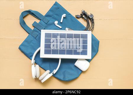 Komposition mit tragbarem Solarpanel, kabellosen Kopfhörern und Tasche auf beigefarbenem Holzhintergrund Stockfoto