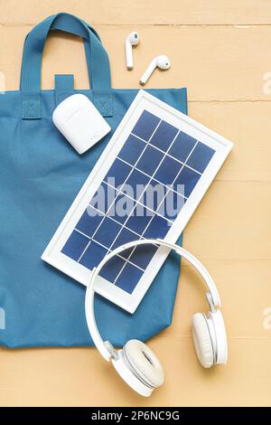 Komposition mit tragbarem Solarpanel, kabellosen Kopfhörern und Tasche auf beigefarbenem Holzhintergrund Stockfoto