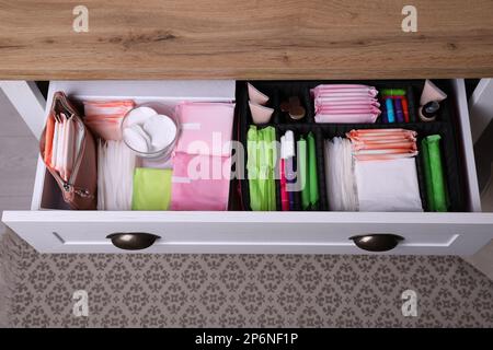 Offene Schublade mit Menstruationseinlagen, Tampons und Hautpflegeprodukten im Innenbereich, über der Ansicht Stockfoto