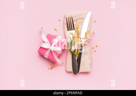 Besteckset mit Mimosablüten in Serviette und Geschenkbox auf pinkfarbenem Hintergrund Stockfoto