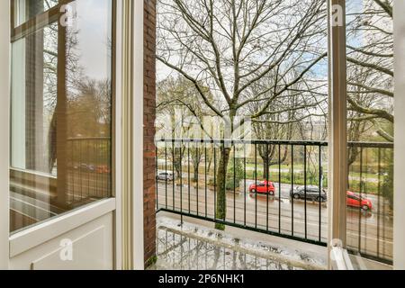 Ein Außenbereich mit Autos, die auf der Straße geparkt sind und Bäume, die sich im Wasser von einem Fenster reflektieren Stockfoto