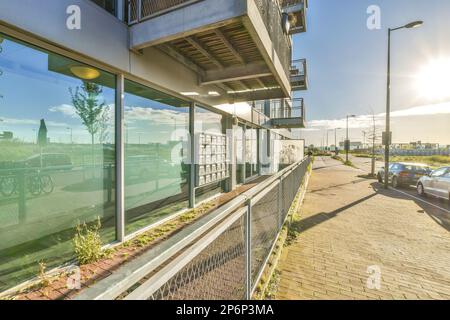 Amsterdam, Niederlande - 10. April 2021: Die Außenseite eines Gebäudes mit Autos, die auf der Straße geparkt sind, und Gebäuden im Hintergrund, die durch Glasfenster gesehen werden Stockfoto