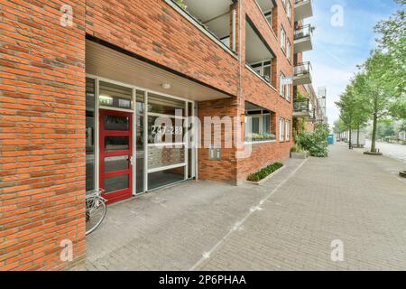 Amsterdam, Niederlande - 10. April 2021: Ein Backsteingebäude mit einem Fahrrad, das in der Tür geparkt ist, und einer offenen roten Tür an der Seite des Gebäudes Stockfoto