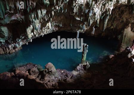 Düstere Aufnahme der Kalkstein-Rangko-Höhle in Labuan Bajo auf Flores mit Stalagtiten von der Decke und einem Höhlensee. Stockfoto