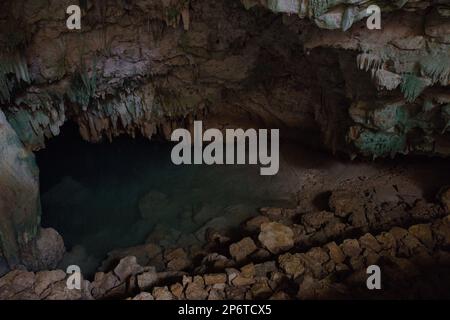 Düstere Aufnahme der Kalkstein-Rangko-Höhle in Labuan Bajo auf Flores mit Stalagtiten von der Decke und einem Höhlensee. Stockfoto