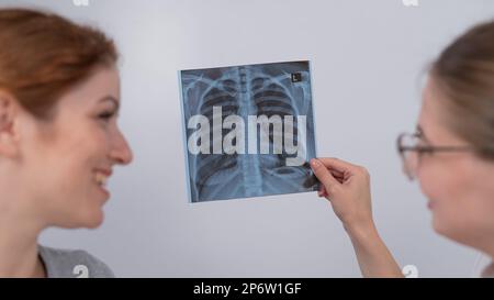 Der Arzt konsultiert eine kaukasische Frau und kommentiert die Röntgenaufnahme der Lunge. Stockfoto