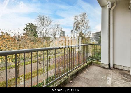 Ein Balkon mit Bäumen im Hintergrund und blauem Himmel darüber, aus dem Balkonfenster eines Apartments Stockfoto