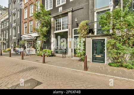 Amsterdam, Niederlande - 10. April 2021: Eine Stadtstraße mit Menschen, die auf Bänken und Tischen in der Mitte der Straße sitzen, umgeben von hohen Ziegelgebäuden Stockfoto