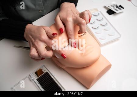 Grundausbildung, Wimpern an einer Schaufensterpuppe aus Silikon zu bauen. Vor der Wimpern-Verlängerung mit Klebeband unter dem Auge arbeiten, Draufsicht. Stockfoto