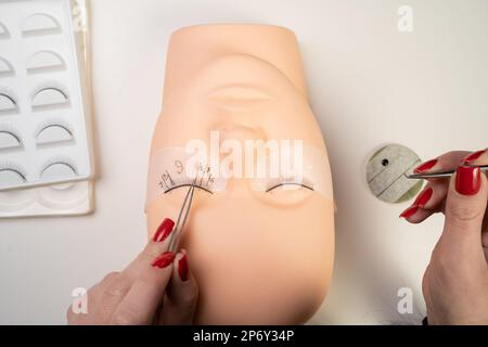 Grundausbildung, Wimpern an einer Schaufensterpuppe aus Silikon zu bauen. Wimpern Nahaufnahme. Arbeiten Sie mit einer Pinzette. Wimpernverlängerung. Stockfoto