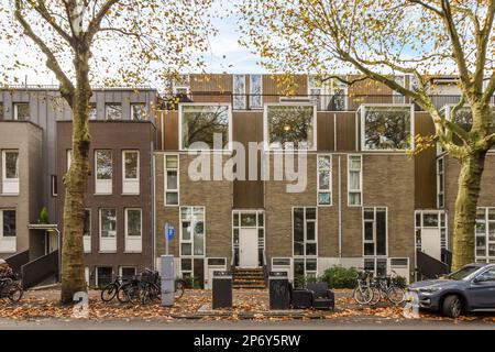 Amsterdam, Niederlande - 10. April 2021: Ein Apartmentkomplex mit Fahrrädern, die auf der Straße davor geparkt sind, und Bäumen, die überall Laub gefallen haben Stockfoto