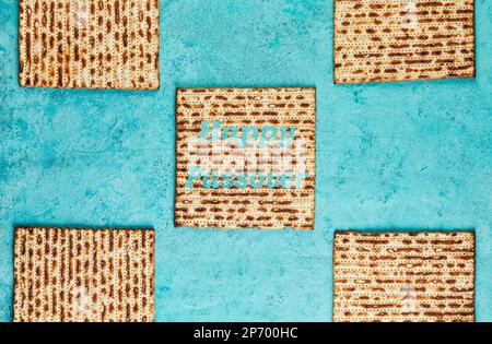 Pesach-Festungskonzept - jüdischer Feiertag Pesach. Matzah-Quadrate, gestapelt in einem Quadrat auf blauem Hintergrund. Frohe Osterschrift auf Matzah. Flach verlegt Stockfoto