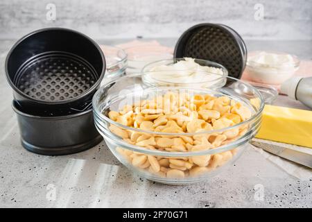 Käsekuchen-Rezept. Drei kleine runde Kuchenpfannen (Dose, Schimmel) und frische Zutaten für das Käsekuchen-Rezept, Nahaufnahme auf dem Küchentisch, flach liegend Stockfoto