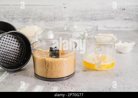 Zerdrückte Cracker, geschmolzene Butter, Frischkäse und einige andere Zutaten für das Käsekuchen-Rezept aus nächster Nähe auf dem Küchentisch Stockfoto